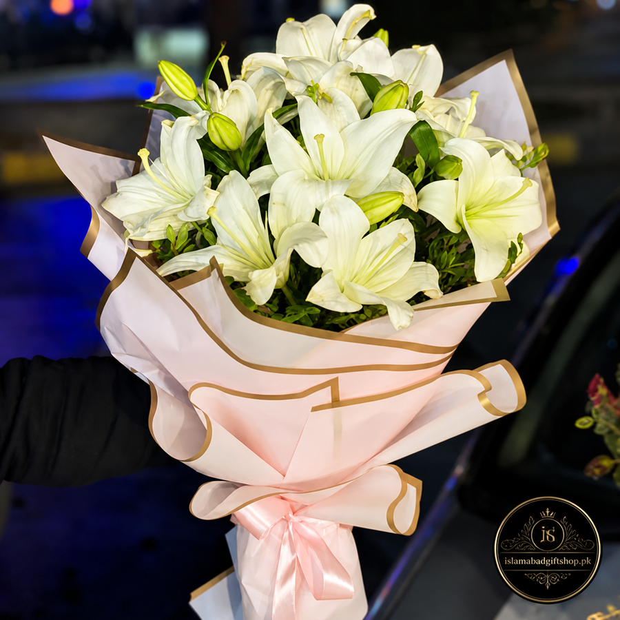 White lily bouquet wrapped in pink paper with gold border, pink ribbon bow.