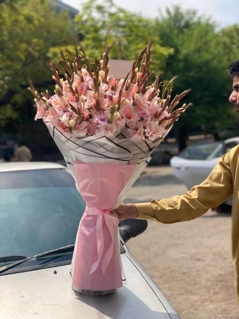 Elegant bouquet of fresh pink gladiolus flowers wrapped in soft pastel paper, arranged as a thoughtful gift for mom.