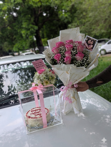 A person holding a large pink rose bouquet next to a white car, featuring an acrylic box with a "Happy Mother's Day" cake and a mother-daughter photo card.