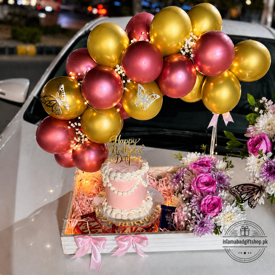 Luxury Mother’s Day gift tray with pink cake, Happy Mother’s Day topper, gold and rose-gold balloon arch, flowers, chocolates, fairy lights.