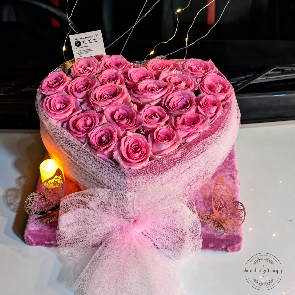 Heart-shaped pink rose arrangement with fairy lights, pink net wrapping, large bow, butterfly decor, candle