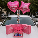 A pink Mother’s Day gift setup displayed on a car hood, featuring a decorative gift box with roses and chocolates, two pink “Happy Mother’s Day” balloons, and a vertical strip of personal photos.